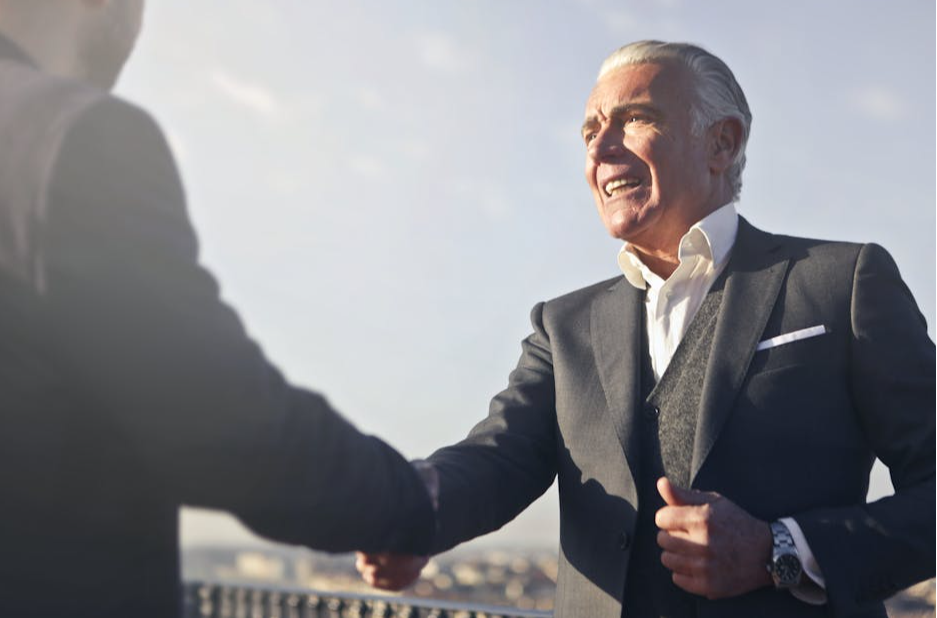 A senior businessman warmly shakes hands outdoors, symbolizing agreement and mutual respect.
